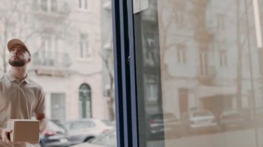 Sıradan üniformalı bir teslimatçı elinde karton bir kutuyla binaya giriyor ve teslimat yapmaya hazır..