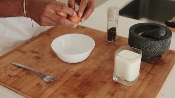 近くの牛乳とスパイスでボウルに卵を割って朝食を準備する認識できない人 — ストック動画