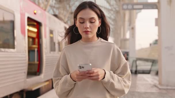 一位年轻女子在火车站台上行走时 专心致志地看着她的智能手机 建议人们进行交流 科技和日常通勤 — 图库视频影像