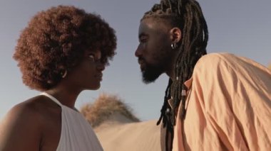 Siyahi bir adam ve Afrikalı bir kadın birbirlerinin gözlerinin içine bakar, dış arkaplana karşı sevgi ve bağlarını ifade ederler..