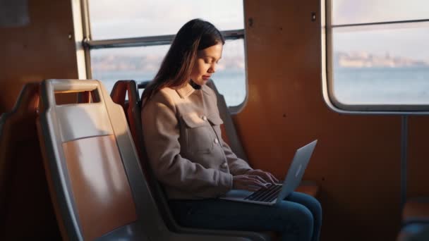 朝の光の中で川を渡るフェリーボートで通勤しながら ノートパソコンに取り組んでいる若い女性 — ストック動画