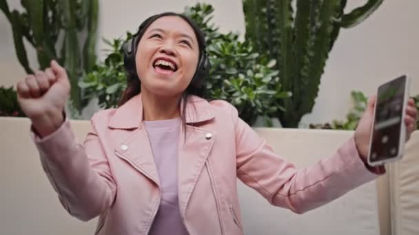 Leende Asiatisk Ung Kvinna Med Hörlurar Dansar Glatt Håller Smartphone — Stockvideo