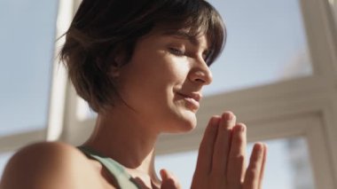 Kapalı gözlü sakin bir kadının yakın çekimi, kapalı mekanda meditasyon yapıyor, güneş ışığı yüzüne sıcak bir ışık saçıyor..