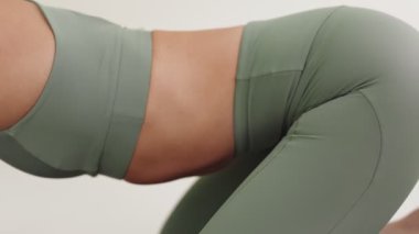Yeşil aktif giysili bir kadının yoga pratiği sırasında çocuk pozu verirken, sakinlik ve esneklik tasvir edişinin yakın çekimi..