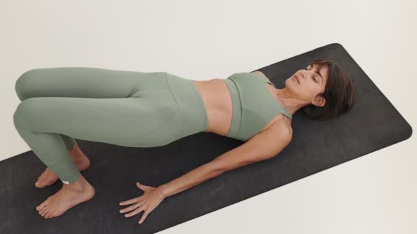 一名专心致志的妇女在一个简约的练习室里 在一个黑色瑜伽垫上做着浮桥运动 展示了她的力量和体形 — 图库视频影像