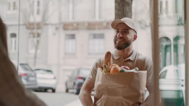 快乐的年轻男性快递员把装满食品杂货的纸袋送到了一位快乐的女性客人家里 — 图库视频影像