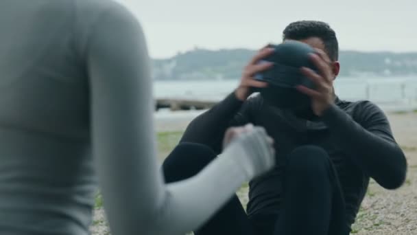 一名年轻的运动员在户外用一个女伴的支持下 用一个健身球扭动着俄罗斯腹肌 这说明了团队合作在健身中的力量 — 图库视频影像