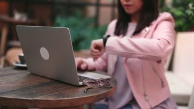 Kafede tanınmayan bir kadın laptopunu toplamadan önce saatine bakıyor. Acil bir durum olduğunu ve geç kalma kavramını somutlaştırıyor..