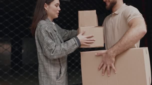 Mężczyzna Beżowej Koszuli Przekazuje Kartonowe Pudełka Uśmiechniętej Kobiecie Przed Siatką — Wideo stockowe