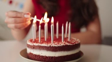 Kutlamaya hazırlanan genç bir kadının yakın çekimi, lezzetli bir doğum günü pastasının üzerinde mum yakması..