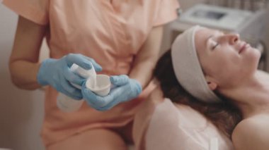 Yetenekli bir kozmetikçi dingin bir güzellik kliniğinde cilt bakımı için yüz maskesi hazırlıyor..