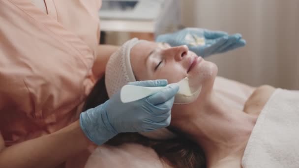 一位戴蓝色手套的美容师在美容院为一位放松的女性顾客轻轻戴上面罩 — 图库视频影像