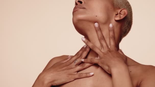 Close-up serene woman with a buzz cut, cradling her neck with a tender touch against a neutral background.