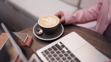 Tanınmayan bir kadın laptopuyla uzaktan çalışırken kahve molası verip kapuçinosunun tadını çıkarıyor..