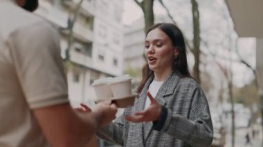 Genç bir kadın, şehir sakinleri arasında kentsel bir teslimatı, rahatlığı ve dostça bir jesti temsil eden açık havada bir kişiden kahve alır..