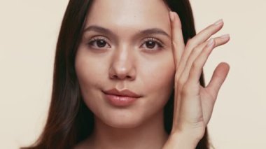 Sakin genç bir kadın, sakin bir ifadeyle ve eli yavaşça yüzünü bej bir zemine dayamış..