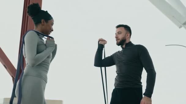 多种族健身双打在室外训练课程 一名中东男子带着抵抗带进行训练 而一名黑人妇女则观察和建议 — 图库视频影像