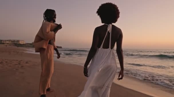 Kochająca Się Czarna Para Trzyma Się Ręce Spacerując Plaży Zachodzie — Wideo stockowe
