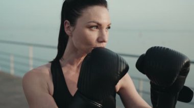Açık havada eldiven eğitimi almış odaklanmış kadın boksör sportif bir antrenman sırasında azim ve güç gösteriyor..