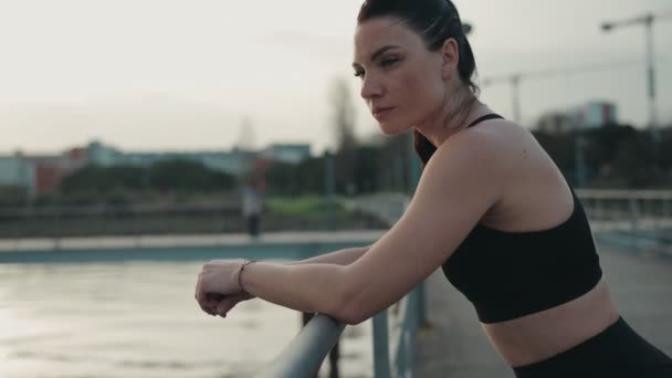 Wanita Atletik Dengan Pakaian Olahraga Bersandar Rel Jembatan Samping Sungai — Stok Video