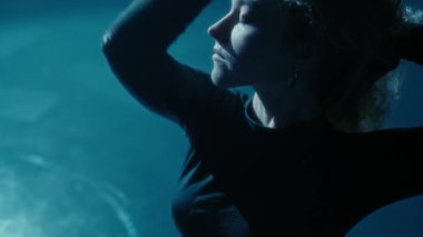 Büyüleyici genç bir kadın, loş bir stüdyoda, hareketleriyle şehvet ve özgürlüğünü ifade ederek zarif bir şekilde dans eder..