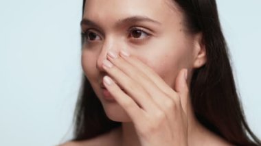 Yüzüne nazikçe dokunan bir kadının elini gösteren detaylı bir yakın plan, cilt bakımı kavramını vurguluyor..