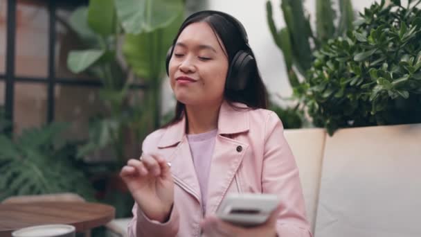 카페에있는 아시아의 여성은 그녀의 헤드폰과 음악을 즐기는 그녀의 스마트 노래를 — 비디오