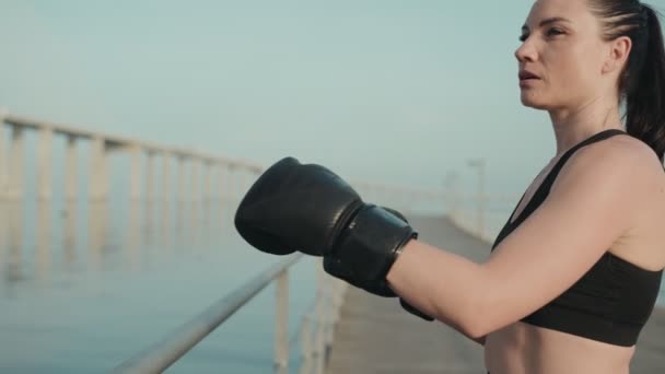 疲惫的女性 戴着拳击手套 靠在桥上的栅栏上 在室外拳击训练中休息片刻 — 图库视频影像