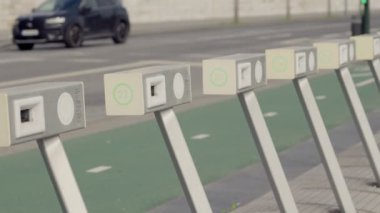 Şehir caddesindeki umumi bisiklet kilitleme istasyonuna bir sıra boş bisiklet yanaşıyor, şehir ulaşımını ve sürdürülebilirliği ima ediyor..