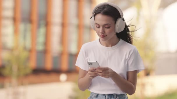 Snygg Ung Kvinna Med Hörlurar Fokuserade Sin Smartphone Mitt Livlig — Stockvideo