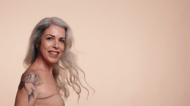 Dövmeli, enerjik, yaşlı bir kadın. Yumuşak bir arka planda, neşe ve kendine güveni ifade ediyor..