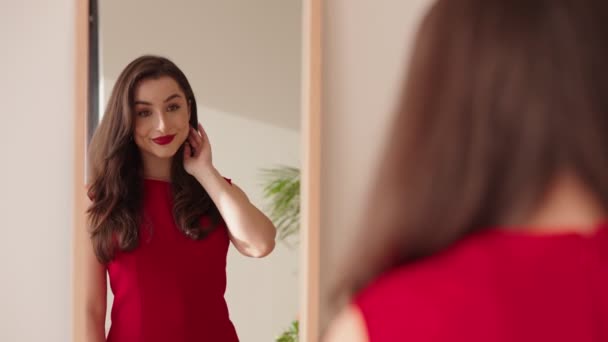 エレガンスと自信を誇る鏡で彼女の反射を見ているリップスティックとイヤリングと赤いドレスのファム脂肪 — ストック動画