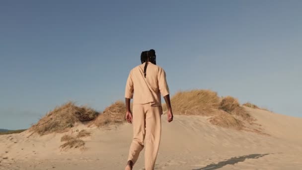 穿着米黄色衣服的孤身一人在沙丘上散步的背影 在晴朗的蓝天下唤起了孤独与宁静 — 图库视频影像