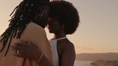Şefkatli bir Afrikalı Amerikalı çift, sakin bir günbatımı ve manzara ile şefkatli bir kucaklaşmayı paylaşıyor, onların arka planı, aşkı ve samimiyeti simgeliyor..