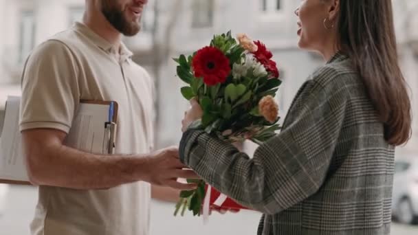 一位高兴的年轻女子收到了一位微笑的男性信使送来的一束美丽的花束 对惊喜送花表示高兴和感谢 — 图库视频影像