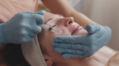 Bir kozmetolojistin yakın çekimi, cilt bakımı sırasında hastaların yüzüne besleyici yağ uygulayan eller.