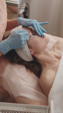 Bir kozmetolojistin cilt bakımı sırasında gevşemiş bir kadının yüzüne yağ sürerken yakın plan görüntüsü..