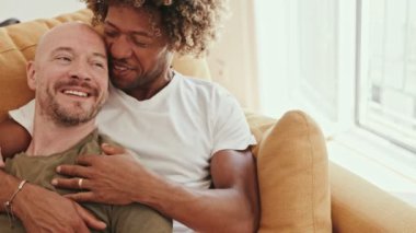 Mutlu eşcinsel çift evde dinleniyor, sıcak bir kucaklaşmayı ve kahkahayı paylaşıyor, birlikte kanepede uzanıyor, sevgi ve çeşitlilik sergiliyorlar..