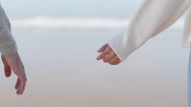 Okyanus kenarında birbirine uzanan genç bir erkek ve kadının ellerini gösteren yakın plan bir resim. Bağlantının ve desteğin sembolü..