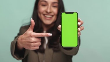 Neşeli genç kadın telefonuna yeşil ekran ile işaret ediyor. Kolay yenisiyle, uygulamayla ya da internet sitesi promosyonu için mükemmel..