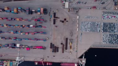 Yığınla renkli konteynır, kenetlenmiş gemiler ve park halindeki araçlarla bir nakliye limanının dinamik ortamını yakalayan bir hava görüntüsü..