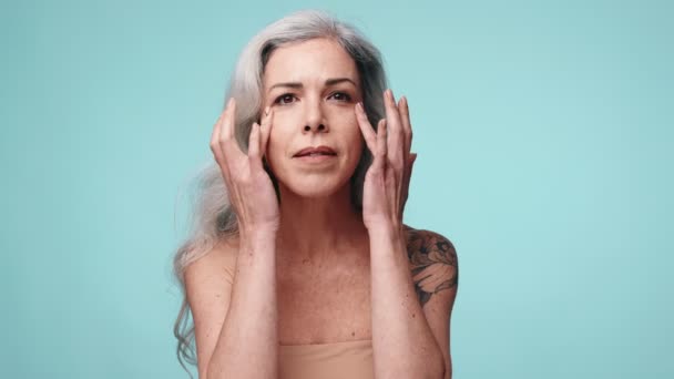 Ηλικιωμένη Κυρία Δείχνει Ρουτίνα Περιποίησης Κάτω Από Μάτια Μπλε Φόντο — Αρχείο Βίντεο