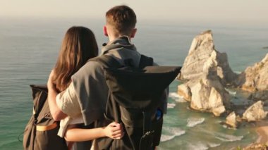 Arka planda birlikte duran genç bir çift yüksek görüş açısıyla büyüleyici bir sahil manzarasına bakıyor..