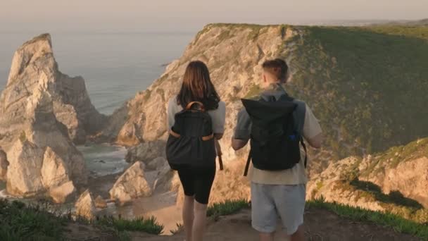 Dwoje Ludzi Plecakami Stojących Klifie Widokiem Ocean Zachodzie Słońca Przechwytujących — Wideo stockowe