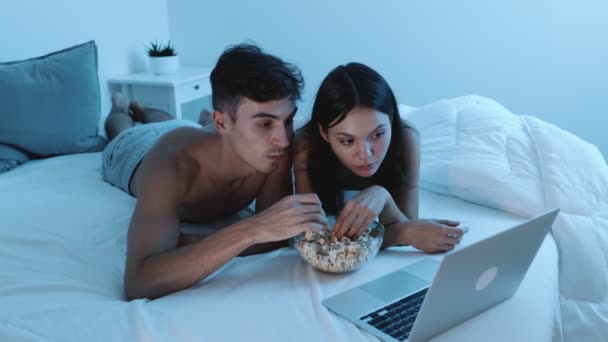 一对夫妇在床上放松一下 一边在笔记本电脑上看电影 一边在晚上吃一碗爆米花 — 图库视频影像