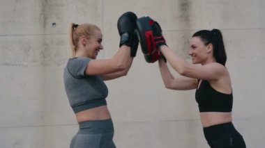 İki atletik kadın güçlü bir jest yaparak beşlik çakıyor. Açık hava boks dersinin başarısını kutluyorlar..