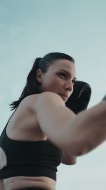 Boks eldivenli kaslı bir kadın spor salonunda yumruk ve tekme pratiği yapıyor..