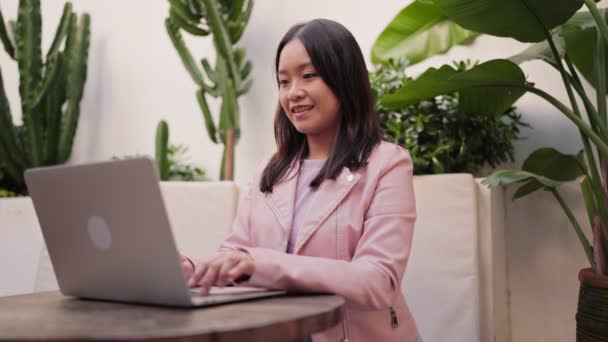 아시아 여자는 식물에 둘러싸인 아늑한 카페에서 그녀의 노트북에 집중적으로 — 비디오