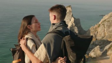 Sırt çantalı genç bir adam ve kadın, okyanusa bakan bir uçurumda samimi bir kucaklaşmayı paylaşıyor. Bir macera ve romantizm anı yakalıyorlar..