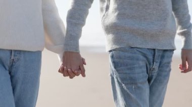 Tanınmayan bir çiftin el ele tutuşup kumsalda birlikte yürüdüğü, aşkı ve arkadaşlığı simgeleyen samimi bir an..